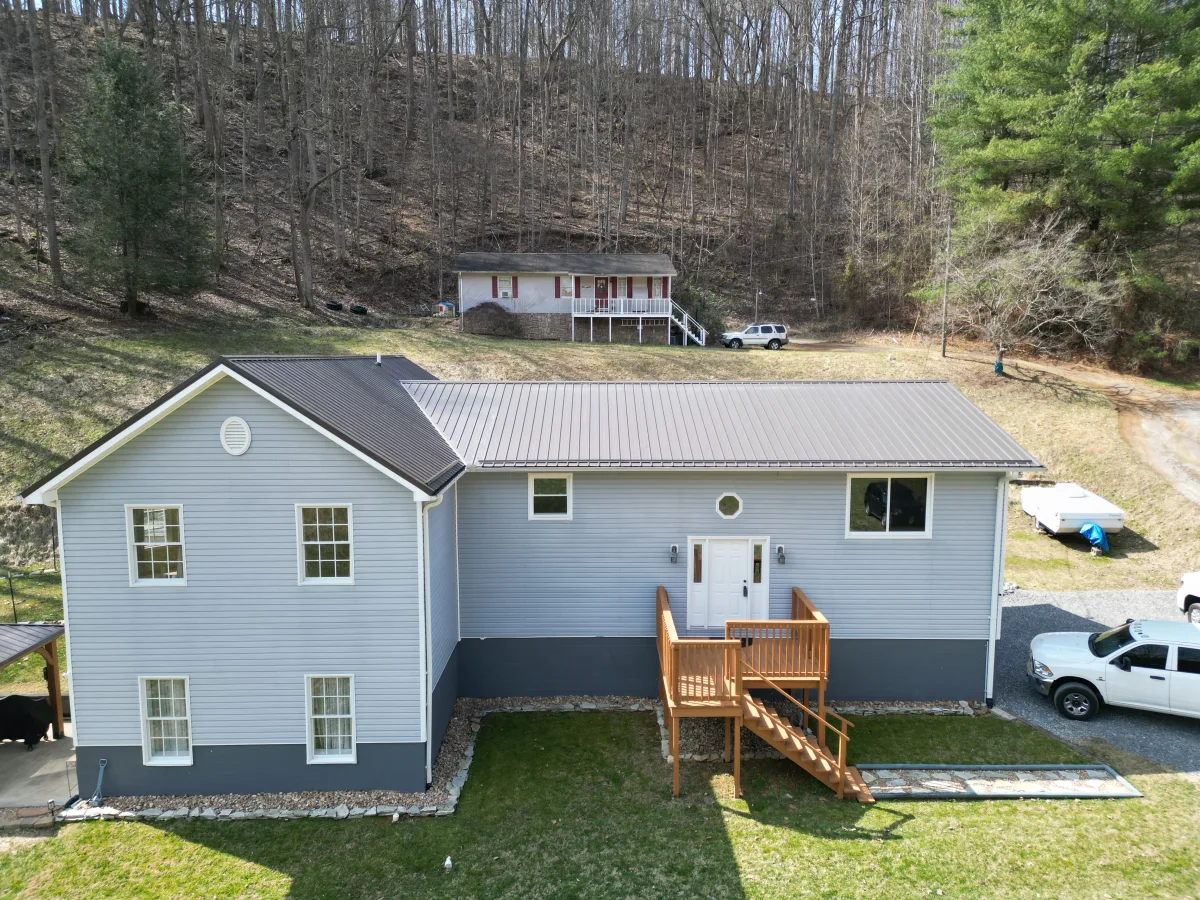 Burnished bronze standing-seam metal roof on a hillside split-level home with gray-blue siding — completed by Palisade Roofing.