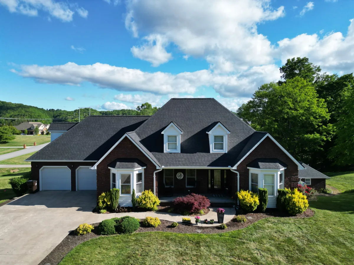 Charcoal architectural shingles on a large brick ranch with dormers and a mountain backdrop — a Palisade Roofing installation in the Tri-Cities.